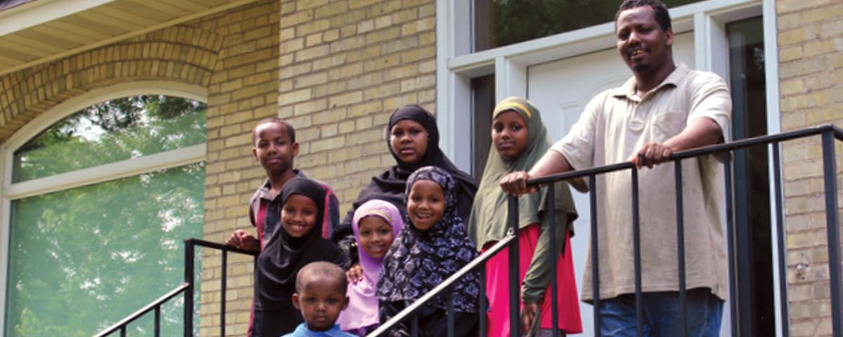 A family of seven on the steps outside a newly purchased brick home