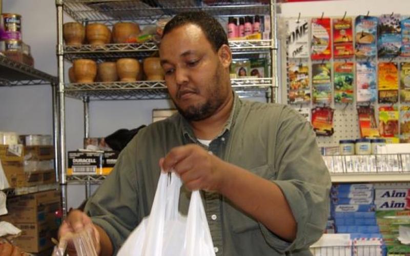 Photo of Abdiqafar Adan bagging a customer purchase in his grocery